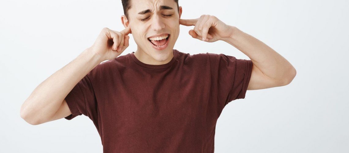Portrait of good-looking childish caucasian guy in red t-shirt, yelling with closed eyes and covering ears with index fingers, not wanting hear girlfriend during fight, standing over gray background, Image: 382505204, License: Royalty-free, Restrictions: , Model Release: yes, Credit line: Profimedia, Stock Budget
