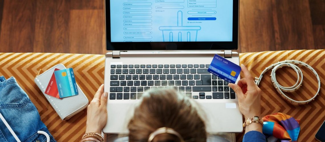 Upper view of young woman in blue blouse with credit card looking at checkout screen on e-commerce website on a laptop while sitting on sofa in the modern living room.,Image: 468462468, License: Royalty-free, Restrictions: , Model Release: no