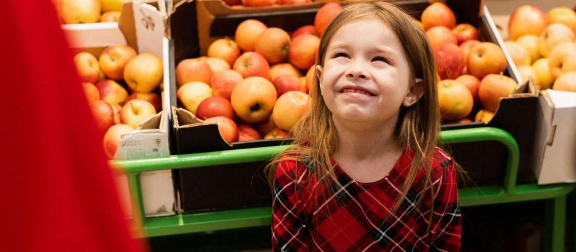 A little girl of about 5 threw a tantrum in a supermarket in front of her parents. The child screams and cries, begging sweets from mom and dad on the background of fruits and apples.,Image: 511595667, License: Royalty-free, Restrictions: , Model Release: yes
